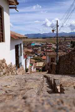 View of the historic cobblestone street in Chinchero with traditional white buildings and stone walls overlooking the town and Andes mountains in Cusco, Cusco, Peru.