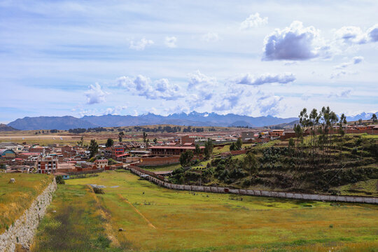 View of the historic town of Chinchero with its traditional stone walls, green fields, and buildings set against the Andes mountains in Chinchero, Cusco, Peru.
