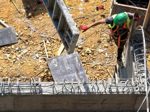 View of a construction worker wearing a green safety helmet and harness maneuvering a concrete formwork panel at a building site in Istanbul, Istanbul, Turkiye.