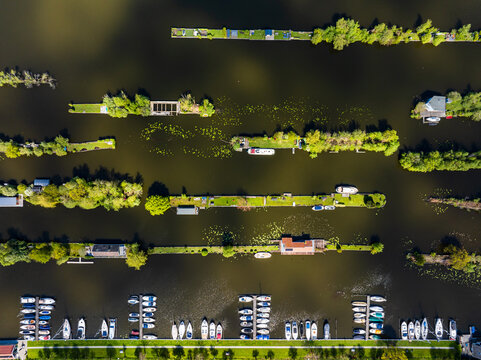 Aerial view of a marina with numerous boats docked in rows, surrounded by small green islands and calm water in Breukeleveen, North Holland, Netherlands.