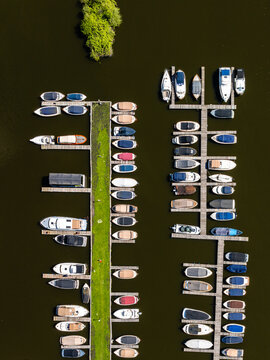 Aerial view of a marina with numerous boats moored along wooden docks, surrounded by calm dark water and a small patch of green vegetation in Breukeleveen, North Holland, Netherlands.