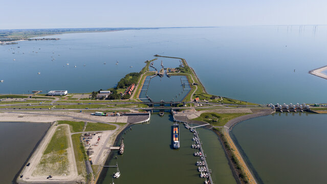 Aerial view of the Kornwerderzand locks and dam with a cargo ship navigating the waterway, surrounded by moored sailboats and the expansive IJsselmeer in Kornwerderzand, Friesland, Netherlands.
