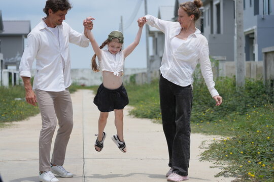 Happy young family with little daughter celebrate as the girl jumps and dad scoops her up on a walk through a new suburban housing development on a bright sunny day