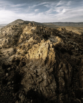 Aerial view of rugged desert rock formations and arid terrain under a soft blue sky in Nevada, United States.
