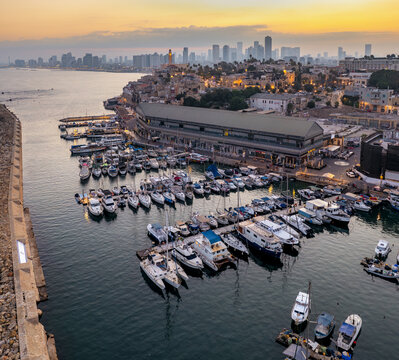 Aerial view of Jaffa Port with boats docked in the harbor, historic buildings, and the Tel Aviv skyline in the background at sunset in Tel Aviv-Jaffa, Tel Aviv District, Israel.