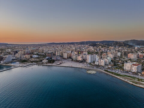 Aerial view of the Vlora coastline featuring urban buildings, sandy beach, and calm sea during golden hour in Vlora, Vlore County, Albania.