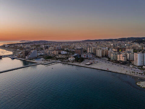 Aerial view of the coastal city of Vlora at sunset, featuring the harbor, sandy beach, and modern buildings along the Adriatic Sea in Vlora, Vlore County, Albania.