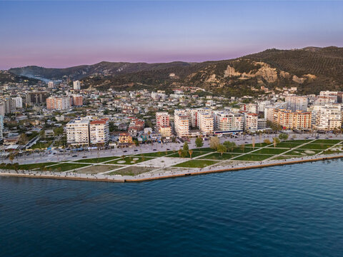 Aerial view of the Vlora waterfront promenade with modern buildings, green spaces, and the coastline at golden hour in Vlora, Vlore County, Albania.