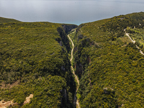 Aerial view of the deep Gjipe Canyon with lush green vegetation on the steep limestone cliffs leading towards the Ionian Sea in Iliaz, Vlore County, Albania.