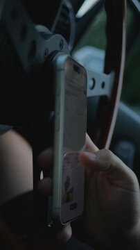 Close-up of tattooed hands scrolling or using a smartphone inside a car, near the steering wheel. Screen is blurred. Mobile communication, digital technology, and online shopping. 4K.