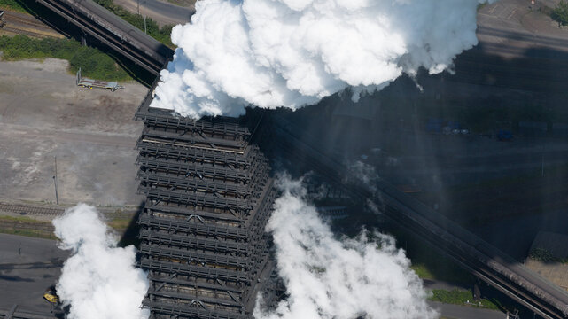 Aerial view of Kokerei Schwelgern coking plant with thick white steam rising from the industrial structure, surrounded by railway tracks in Duisburg, North Rhine-Westphalia, Germany.