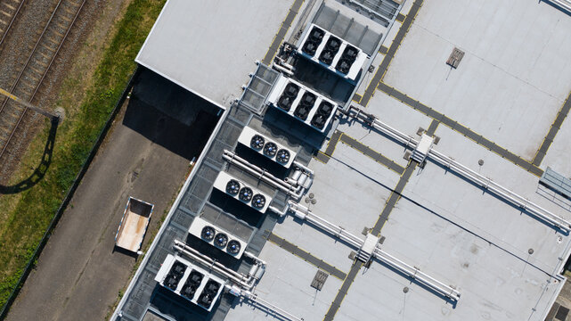 Aerial view of industrial building roof featuring multiple HVAC cooling units and ventilation pipes adjacent to a railway track in Nieuwegein, Utrecht, Netherlands.