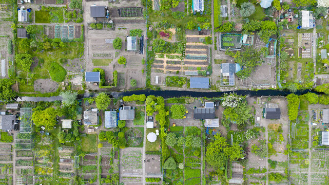 Aerial view of allotment gardens with small greenhouses, sheds, and cultivated plots separated by a narrow canal in De Bilt, Utrecht, Netherlands.