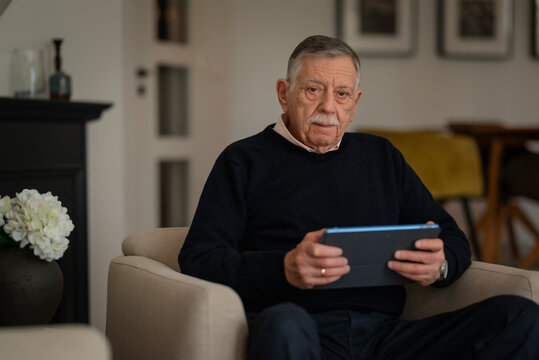 An older man with touchpad sitting in an armchair and checking finances online at home