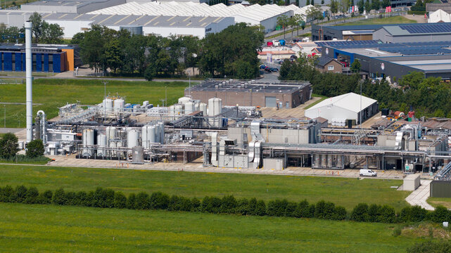 Aerial view of industrial facility featuring large storage tanks, complex piping systems, and storage containers in a paved yard in Zaltbommel, Gelderland, Netherlands.