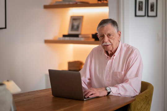 Confident senior man sitting at desk and using laptop in cozy scandinavian style home