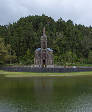 Aerial view of Ermida de Nossa Senhora das Vitorias situated by the lake surrounded by lush forest with people standing near the stone walls in Furnas, Acores, Portugal.