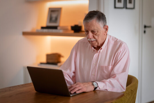Confident senior man sitting at desk and using laptop in cozy scandinavian style home