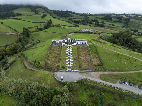 Aerial view of the Chapel of Nossa Senhora da Paz with its iconic long staircase, surrounded by lush green hills and fields in Vila Franca Do Campo, Acores, Portugal.