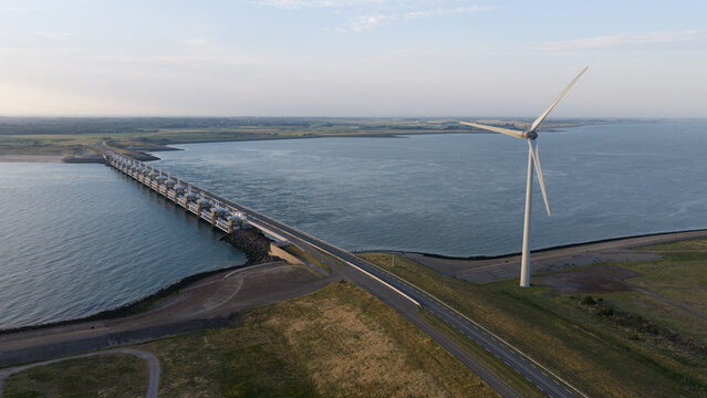 Aerial view of the Eastern Scheldt Storm Surge Barrier with a large wind turbine standing on the coast in Vrouwenpolder, Zeeland, Netherlands.