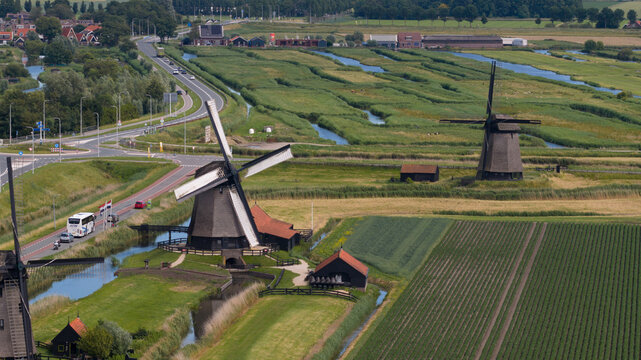 Aerial view of historic windmills in Schermerhorn, surrounded by lush green fields, irrigation canals, and a winding road in Schermerhorn, North Holland, Netherlands.