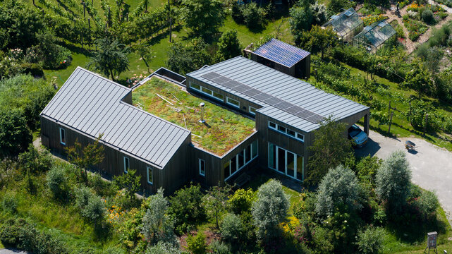 Aerial view of Ecodorp Bolderburen, a modern house with a green sedum roof and solar panels, surrounded by lush gardens, trees, and greenhouses in Almere, Flevoland, Netherlands.