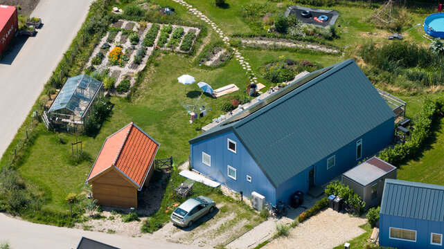 Aerial view of Ecodorp Bolderburen featuring a blue house with solar panels, a greenhouse, a vegetable garden, and a small wooden shed in Almere, Flevoland, Netherlands.