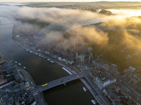 Aerial view of the Collegiate Church of Our Lady of Dinant and the Meuse River at sunrise with mist rolling over the historic town in Dinant, Wallonia, Belgium.