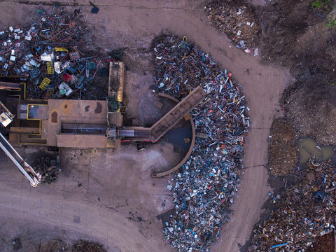 Aerial view of a scrap metal recycling facility with large piles of sorted metal, industrial machinery, and a conveyor belt in Charleroi, Wallonia, Belgium.