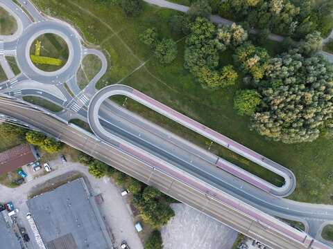 Aerial view of a modern pedestrian and bicycle bridge with a distinctive loop design, surrounded by green spaces and a roundabout in Poland.