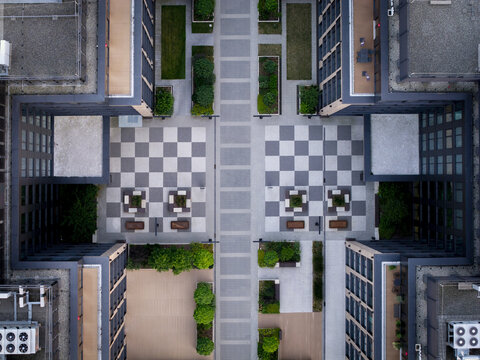 Aerial view of a modern residential complex with a checkered courtyard, landscaped green spaces, and geometric building architecture in Poland.