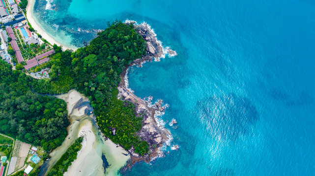 Aerial view of Grand'Anse Mahe coastline featuring a rocky headland covered in lush tropical vegetation, a sandy beach, and clear turquoise ocean waters in Grand'Anse Mahe, Seychelles.