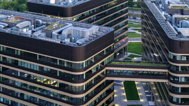 Aerial view of modern office buildings with glass facades, dark horizontal bands, green roofs, and a connecting bridge in Poland.