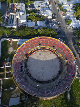 Aerial view of Plaza de Toros Merida showing the circular arena with red and yellow seating tiers surrounded by urban streets and lush trees Merida, Yucatan, Mexico.