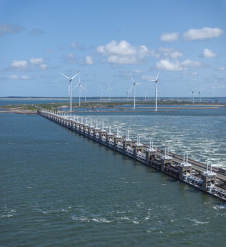 Aerial view of the Eastern Scheldt Storm Surge Barrier with wind turbines in the background, surrounded by the North Sea in Vrouwenpolder, Zeeland, Netherlands.