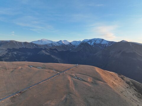 Aerial view of the Sibillini Mountains with snow-capped peaks and a winding road traversing the grassy slopes in Montemonaco, Marche, Italy.