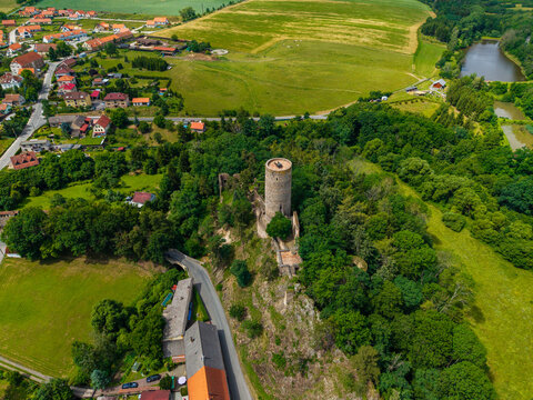 Aerial view of Tocnik Castle surrounded by lush green forests, rolling fields, and the nearby village in Tocnik, Stredocesky kraj, Czechia.