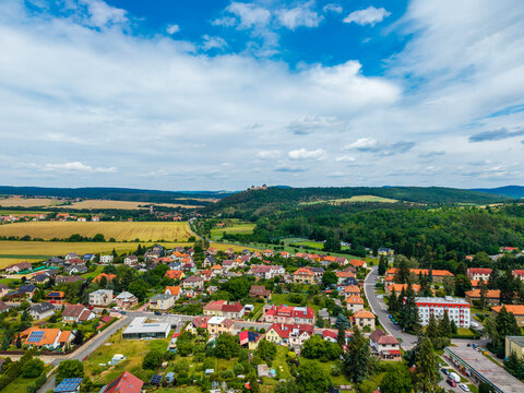 Aerial view of Tocnik Castle overlooking the village with surrounding fields, forests, and residential houses under a blue sky in Tocnik, Stredocesky kraj, Czechia.