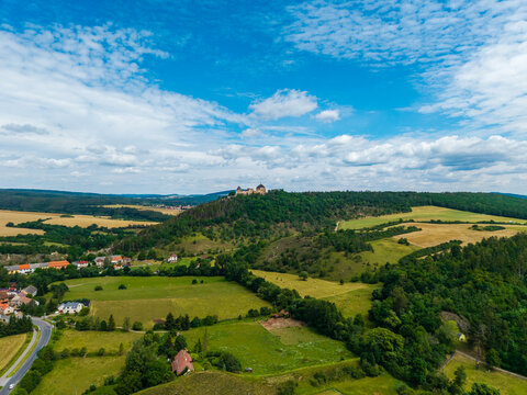 Aerial view of Tocnik Castle perched on a forested hill, surrounded by green fields and rural houses under a blue sky in Tocnik, Stredocesky kraj, Czechia.
