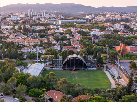 Aerial view of the outdoor stage setup at Parque Carmona surrounded by lush trees and residential buildings in Cascais, Lisboa, Portugal.