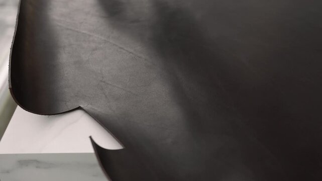 Craftsman measuring black leather with ruler for cutting in a workshop. Professional leatherworking process for custom goods