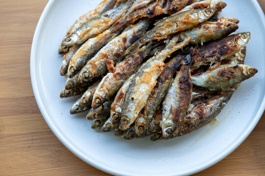 Crispy fried small river fish served on a white plate outdoors during a summer meal. Delicious traditional seafood lunch in a sunny garden.