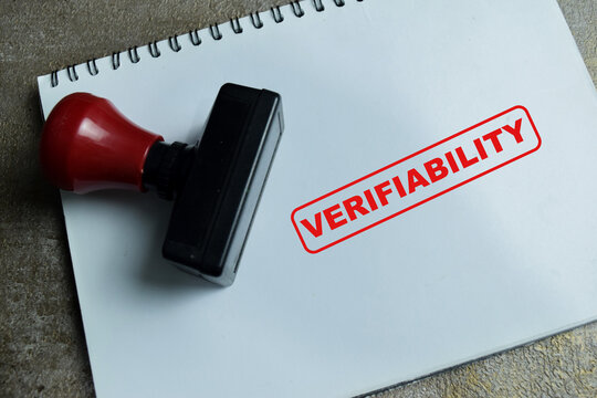 Red Handle Rubber Stamper and verifiability text above book isolated on wooden background. For AI authenticity and trust