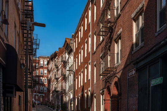 A small alleyway flanked by classic red brick residential buildings with fire escapes in the historic North End neighborhood of Boston, an area also known as Little Italy.