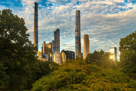 Sunrise view of midtown Manhattan skyline from Central Park featuring tall slender skyscrapers along Billionaires Row illuminated by early morning sunlight in New York City.