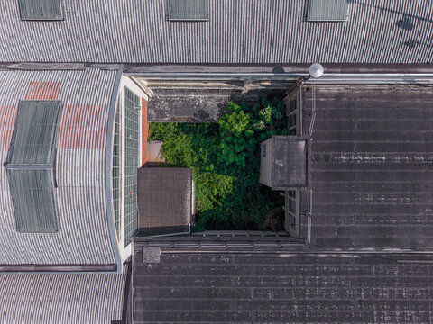 Aerial view of a building rooftop with a central courtyard filled with lush green trees, surrounded by corrugated metal and flat roofing materials in Casale Monferrato, Piedmont, Italy.