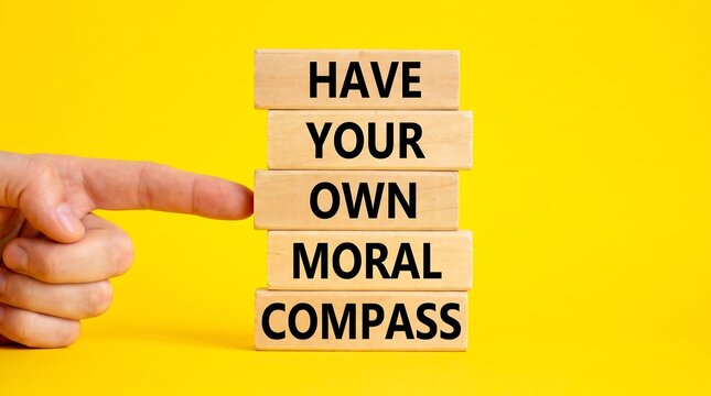 Moral compass concept on wooden blocks, ethical decision making and integrity message, hand pointing to inspirational text on yellow background
