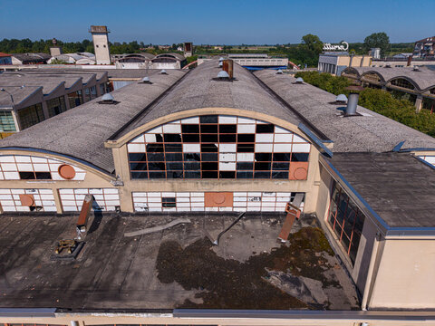 Aerial view of an abandoned industrial factory building with a distinctive arched roof, broken windows, and weathered surfaces in Casale Monferrato, Piedmont, Italy.
