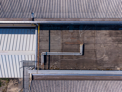 Aerial view of industrial building roof with corrugated metal panels, metal pipes, and a walkway in Casale Monferrato, Piedmont, Italy.