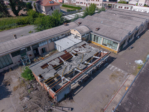 Aerial view of an abandoned industrial building with a partially collapsed roof and surrounding paved yard in Casale Monferrato, Piedmont, Italy.
